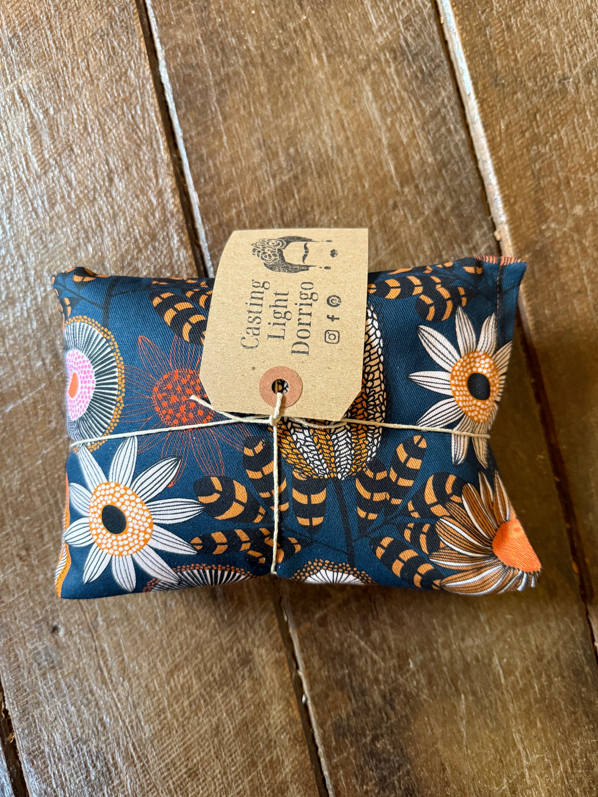 Folded fabric pouch with floral pattern and tag on a wooden surface