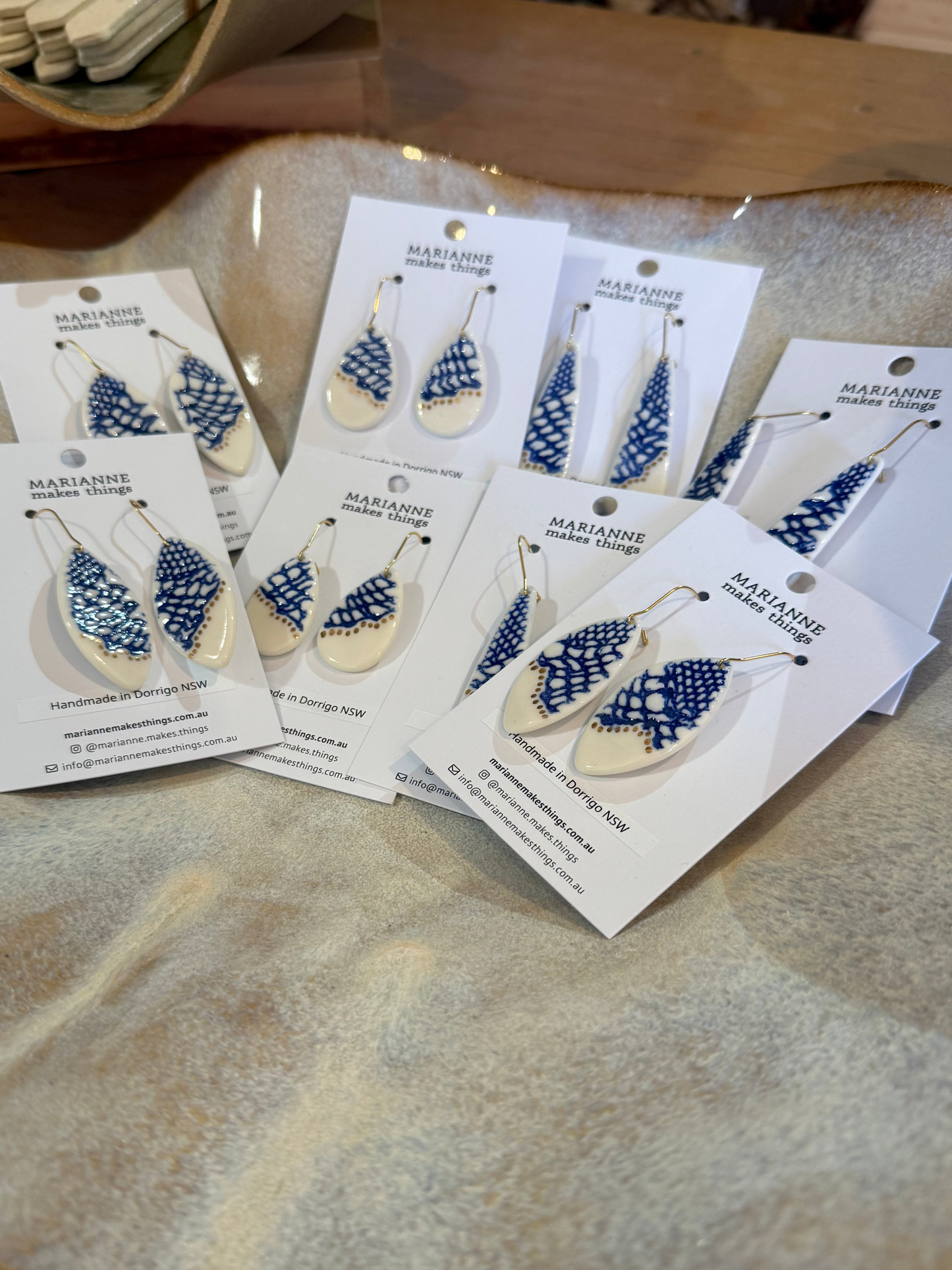 Several pairs of blue and cream beaded dangle earrings on white display cards, arranged on a textured beige ceramic tray.