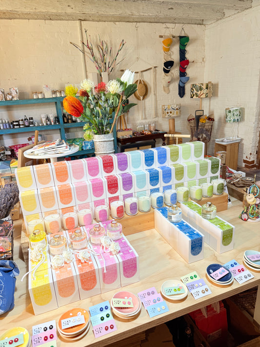 Display of colorful products on a table in a store setting with shelves and decor in the background.